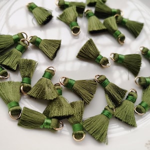 May include: A collection of green tassel charms with gold jump rings. The tassels are made of soft, silky fabric and have a fringed edge.