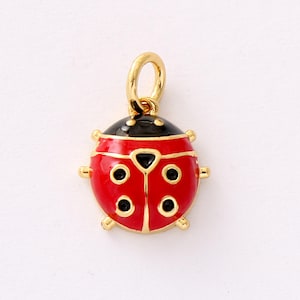 Puede incluir: Un dije de mariquita de color dorado con cuerpo rojo, cabeza negra y puntos negros. El dije tiene un lazo dorado para sujetarlo a un collar o pulsera. La mariquita tiene detalles dorados.