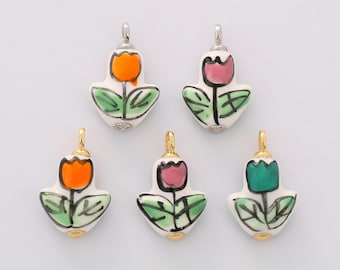 May include: Five ceramic tulip pendants with silver and gold-colored findings. Each pendant features a different colored tulip: orange, pink, and green. The tulips have green leaves and black outlines, set against a white background.