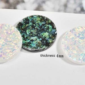 Op de afbeelding: Drie ronde, decoratieve, iriserende onderzetters van hars. De onderzetters zijn 8,9 cm in diameter en 1 cm dik. Eén onderzetter is wit met iriserende vlekken, één is zwart met groen-iriserende vlekken en één is wit met iriserende vlekken.