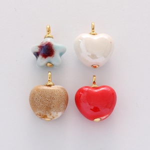 Peut inclure: Quatre pendentifs en céramique en forme d'étoile et de cœurs. L'étoile est bleu clair avec des accents rouges et blancs. Les cœurs sont blancs, marron et rouges. Chaque pendentif a une bélière dorée.