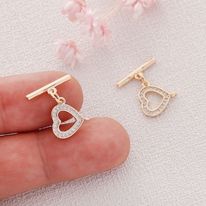 May include: Two gold-tone toggle clasps with clear crystal heart charms. Each clasp has a bar that slides through a loop to secure a necklace or bracelet.