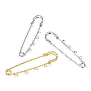 May include: Three safety pins with jump rings. Two silver safety pins and one gold safety pin.