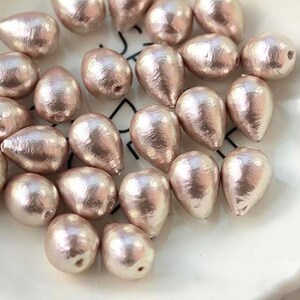 Puede incluir: Una colecci&oacute;n de cuentas de color rosa nacarado en forma de l&aacute;grima, dispuestas sobre una superficie blanca.