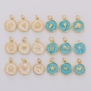 May include: A selection of gold-coloured pendants with marine-themed designs. The pendants feature seashells, starfish, and other sea life, with some having a white or turquoise enamel background. Each pendant has a small loop for attaching to a chain or bracelet.