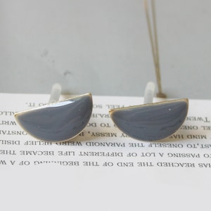 May include: A pair of gray half-circle earrings with gold accents. The earrings are on a white surface with text.