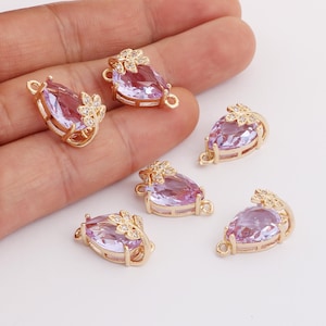 May include: Five gold-tone teardrop-shaped pendant charms with clear purple crystal stones and gold-tone leaf accents. Each charm has a loop at the top for attaching to a necklace or bracelet.