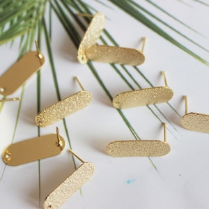 May include: A set of eight gold-toned earring blanks with a textured finish. The blanks are oval-shaped and have a small loop at the top for attaching earring wires.