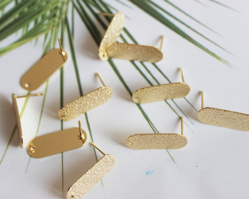 May include: A set of eight gold-toned earring blanks with a textured finish. The blanks are oval-shaped and have a small loop at the top for attaching earring wires.