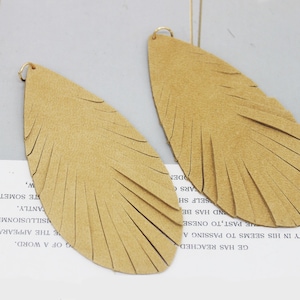 May include: A pair of brown suede feather earrings with gold hoops. The earrings are shaped like teardrops and have a fringe design.