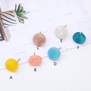 Puede incluir: Surtido de seis pendientes redondos de colores con postes plateados. Los pendientes son de los siguientes colores: amarillo, rosa, marrón, azul, blanco y azul verdoso.