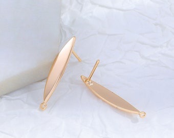 May include: Two gold-colored, elongated oval earring components with a post and a small loop at the base. The earrings are displayed on a white, textured surface. The design is simple and elegant, suitable for jewelry making.