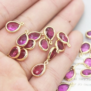 Puede incluir: Un grupo de 14 abalorios de forma de lágrima de color dorado con acentos de cristal rosa. Los abalorios tienen un bucle en la parte superior para sujetarlos a joyas.