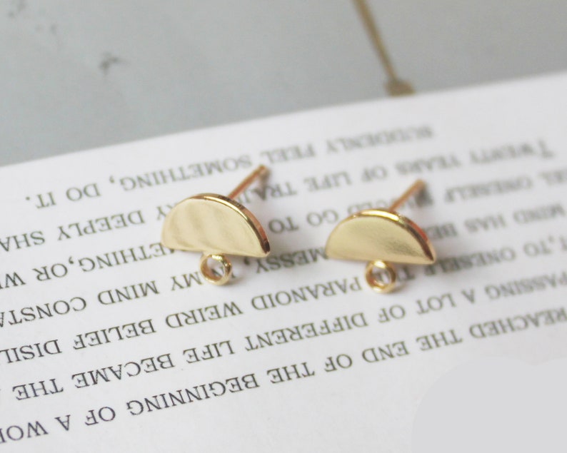 May include: Two gold-toned half-circle earring findings with a small clear bead on the loop of each finding.