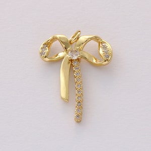 Op de afbeelding: Gouden boog hanger met heldere kristallen accenten. De boog is met een enkele knoop gebonden en heeft een lange, dunne staart.