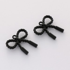 May include: Two black metal bow charms with a rope-like design. The bows have a loop at the top for attaching to a necklace or bracelet.