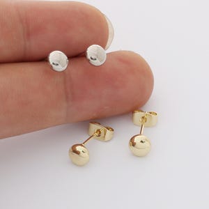 Peut inclure: Deux paires de petites boucles d'oreilles à clous, rondes et polies. Une paire est de couleur argentée et l'autre de couleur dorée. Chaque boucle d'oreille présente une face circulaire lisse avec une tige fine et un fermoir papillon assorti.