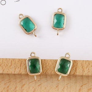 May include: Four gold-toned metal charms with green glass square-shaped stones. Each charm has a loop at the top and a hook at the bottom.