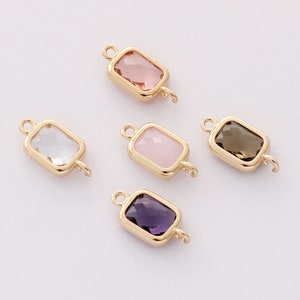 Peut inclure: Cinq breloques en métal doré avec des inserts en verre de différentes couleurs. Les breloques sont rectangulaires avec des coins arrondis et ont une boucle à chaque extrémité. Les inserts en verre sont transparents, roses, violet clair, bruns et violet foncé.