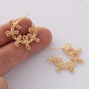 May include: A pair of gold hoop earrings with a delicate, intricate design. The earrings are made of thin, twisted wire that forms a circular shape with a floral pattern.