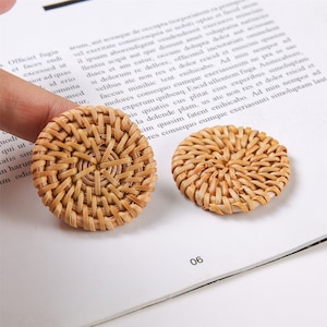 May include: Two round, woven, light brown wicker earrings. The earrings are made of natural materials and have a simple, elegant design.