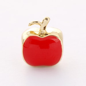 May include: A gold charm in the shape of a red apple. The apple has a gold stem and leaf.