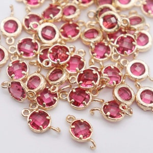 May include: A pile of gold-toned metal charms with pink glass accents. Each charm has a round shape with a loop on the top and a smaller loop on the side.