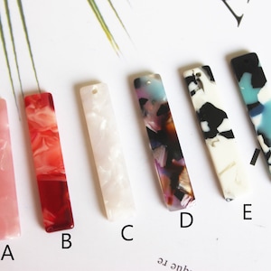 Puede incluir: Seis diferentes abalorios rectangulares de acrílico con patrones de mármol en rosa, rojo, blanco, multicolor, blanco y negro y azul. Los abalorios están etiquetados de la A a la F.