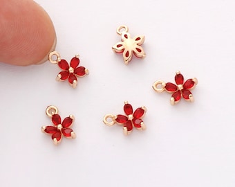 May include: Five gold-tone flower charms with red crystal accents. The charms have a loop at the top for attaching to jewelry.
