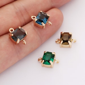 Puede incluir: Cuatro conectores de metal dorado con piedras de cristal facetadas de forma cuadrada. Las piedras son azules, grises, verdes y marrones.