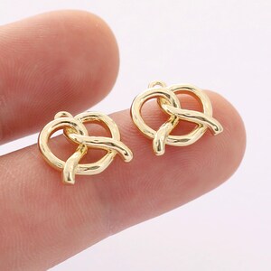 May include: Two gold-colored metal charms shaped like pretzels. The charms have a loop at the top for attaching to jewelry or other crafts.
