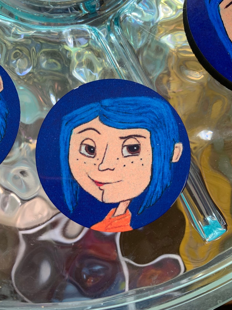 May include: A round blue and white sticker with a cartoon illustration of a girl with blue hair and freckles. She is wearing an orange shirt.