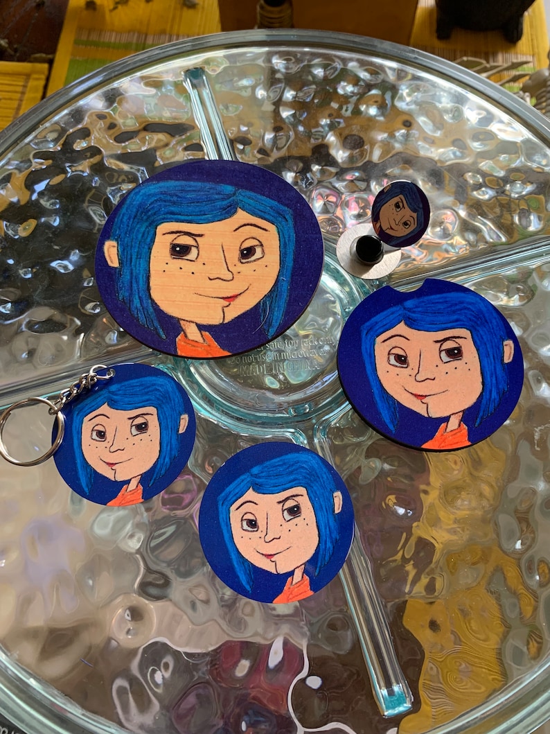May include: Set of four round coasters featuring a cartoon character with blue hair and a red dress. The coasters are made of wood and have a dark blue background. The character is from the movie "Coraline".