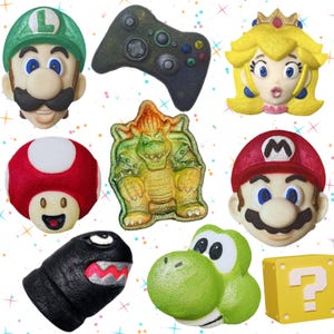 May include: A collection of colorful, sculpted bath bombs featuring characters and icons from the Super Mario video game series. Includes Mario, Luigi, Princess Peach, Yoshi, a controller, and a question mark block.