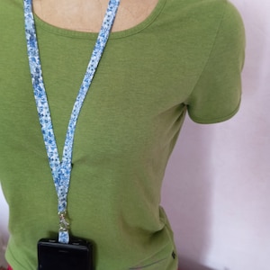 Peut inclure: Un t-shirt vert avec un cordon bleu et blanc à motifs attaché à un étui de téléphone noir.