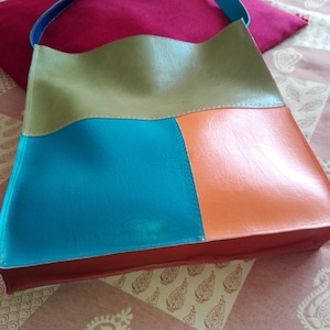 Peut inclure: Un sac fourre-tout en cuir multicolore avec un schéma de couleurs vert, bleu, orange et rouge. Le sac a une seule sangle et est fait d'un patchwork de pièces de cuir de différentes couleurs.