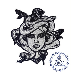 Könnte beinhalten: Schwarz-weiß gestickter Patch von Medusa mit Schlangen als Haar. Der Patch zeigt ein detailliertes Design von Medusas Gesicht und Schlangen. Der Text "Taiss Embroidery" ist in einem Kreis unter dem Patch sichtbar.