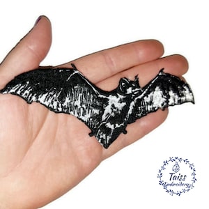 May include: Black and white embroidered iron-on patch of a bat with wings spread. The patch is about 3 inches wide.