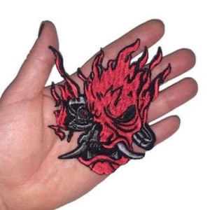 May include: Red and black embroidered iron-on patch of a flaming demon mask.