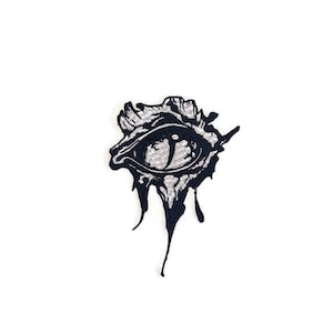May include: A black and white embroidered patch of an eye with dripping black ink.