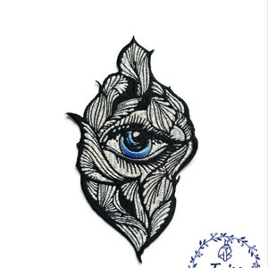 Peut inclure: Patch brodé noir et blanc avec un motif d'œil détaillé. L'œil a un iris bleu et une pupille noire. Le patch a la forme d'une larme et a un fond blanc.
