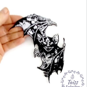 Puede incluir: Parche de hierro bordado en blanco y negro de un murciélago con las alas extendidas. El murciélago está en una pose amenazante con los dientes descubiertos. El parche es perfecto para agregar un toque espeluznante a la ropa, las bolsas u otros accesorios.