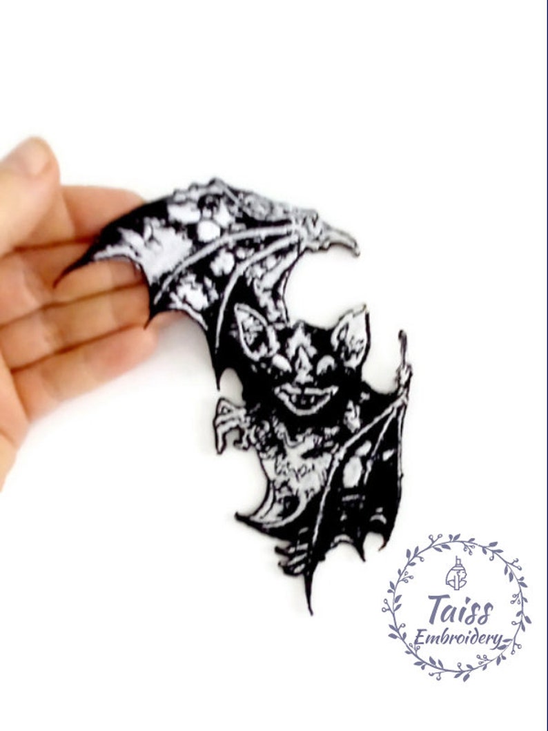 May include: Black and white embroidered iron-on patch of a bat with wings spread. The bat is in a menacing pose with its teeth bared. The patch is perfect for adding a spooky touch to clothing, bags, or other accessories.