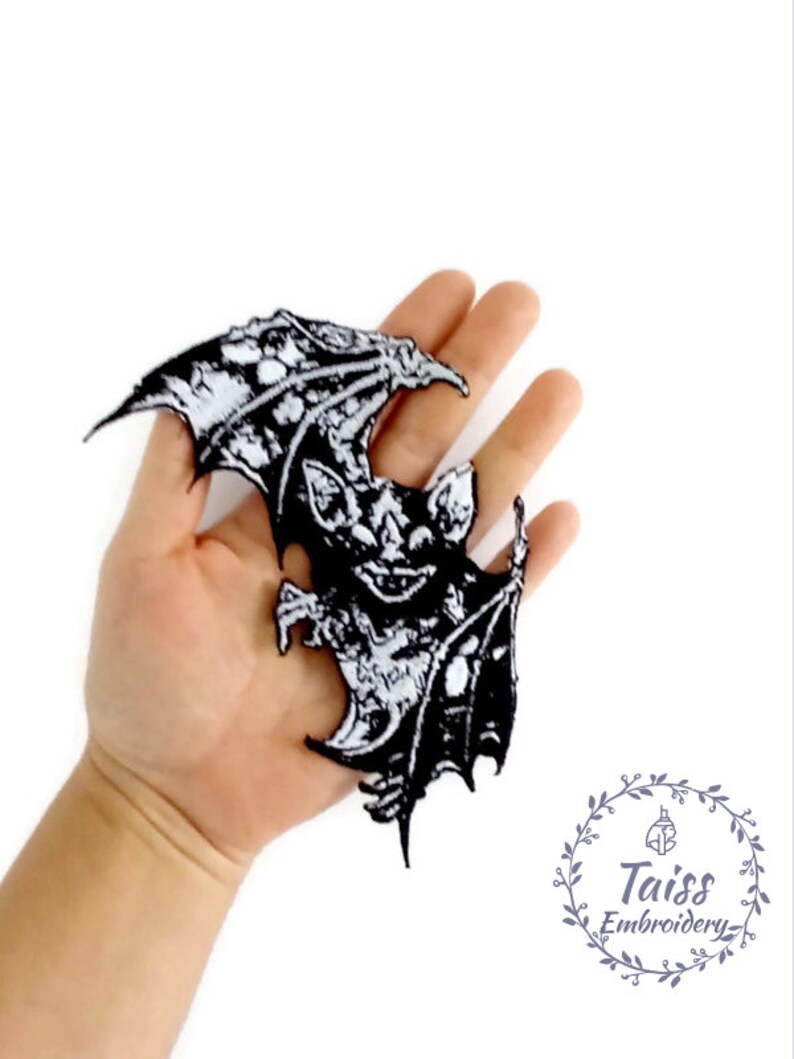 May include: Black and white embroidered iron-on patch of a bat with wings spread. The bat has a detailed design with a menacing expression. The patch is perfect for adding a spooky touch to clothing, bags, or other accessories.