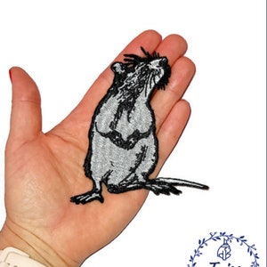 Pode incluir: Patch bordado com um rato estilizado em tons de cinza e preto. O rato é retratado numa pose detalhada, olhando para cima. O patch é provavelmente projetado para aplicação em roupas ou acessórios. O logotipo Taiss Embroidery é visível.