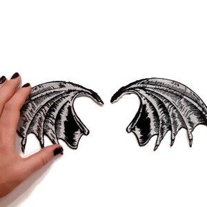 K&ouml;nnte beinhalten: Ein Paar schwarze und silberne gestickte Fl&uuml;gel. Die Fl&uuml;gel sind so gestaltet, dass sie wie D&auml;monenfl&uuml;gel aussehen.