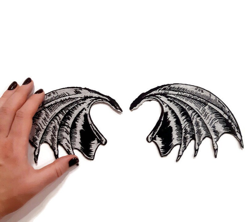 K&ouml;nnte beinhalten: Ein Paar schwarze und silberne gestickte Fl&uuml;gel. Die Fl&uuml;gel sind so gestaltet, dass sie wie D&auml;monenfl&uuml;gel aussehen.