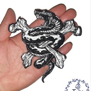 May include: Black and white embroidered iron-on patch featuring a snake wrapped around crossed bones.