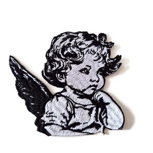 May include: Embroidered patch featuring a cherub with a single wing. The design is in black and white, with the cherub's face turned to the side. The patch is likely for clothing or accessories.