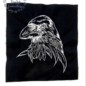 May include: White embroidered raven head on a black fabric background.